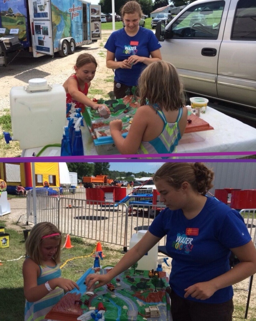 Megan Koppenhafer, fellow intern, adding loose soil to the watershed, with an eager repeat visitor (in stripes), at the Audubon County Fair.